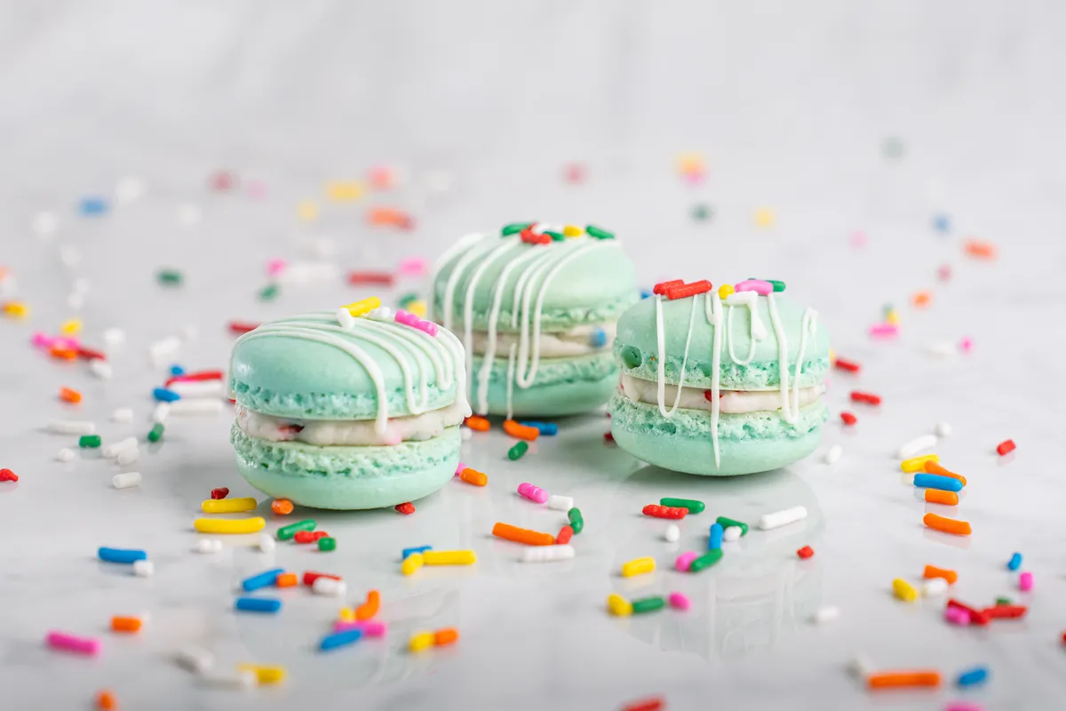 Mint green birthday cake macarons with white drizzle and rainbow sprinkles