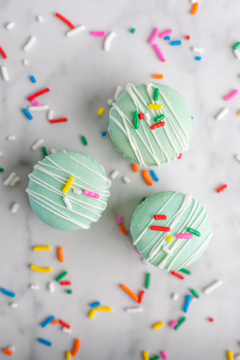 Mint green birthday cake macarons with white drizzle and rainbow sprinkles
