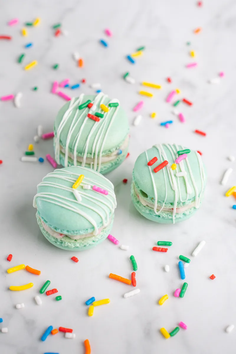 Mint green birthday cake macarons with white drizzle and rainbow sprinkles
