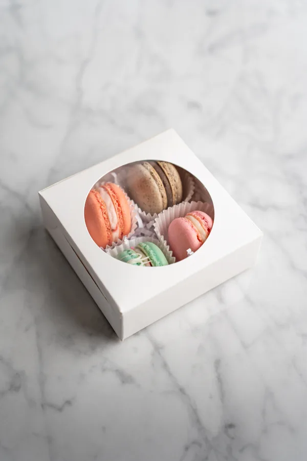 A box of assorted Baked by Brook macarons on white marble
