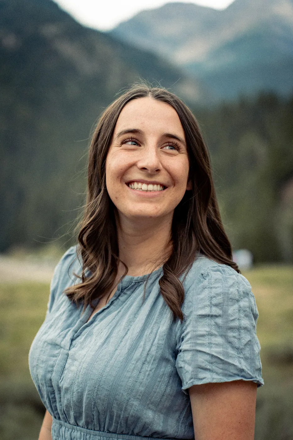 Brook smiling and looking up, outdoors in front of a mountain landscape