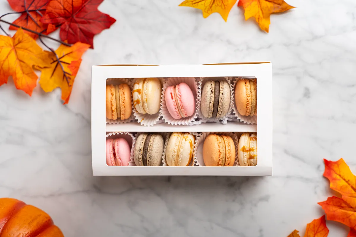 A flat lay of a boxed macaron assortment framed by autumn leaves