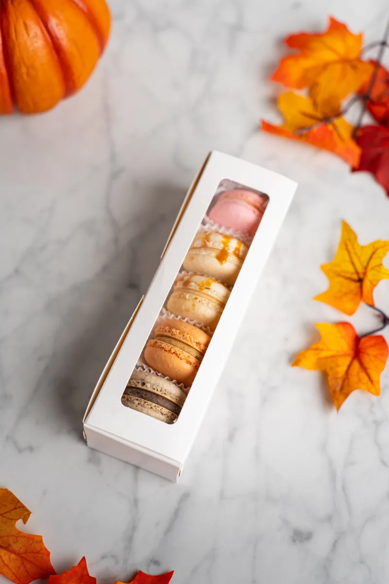 A sampler box of macarons with autumn leaves and a pumpkin
