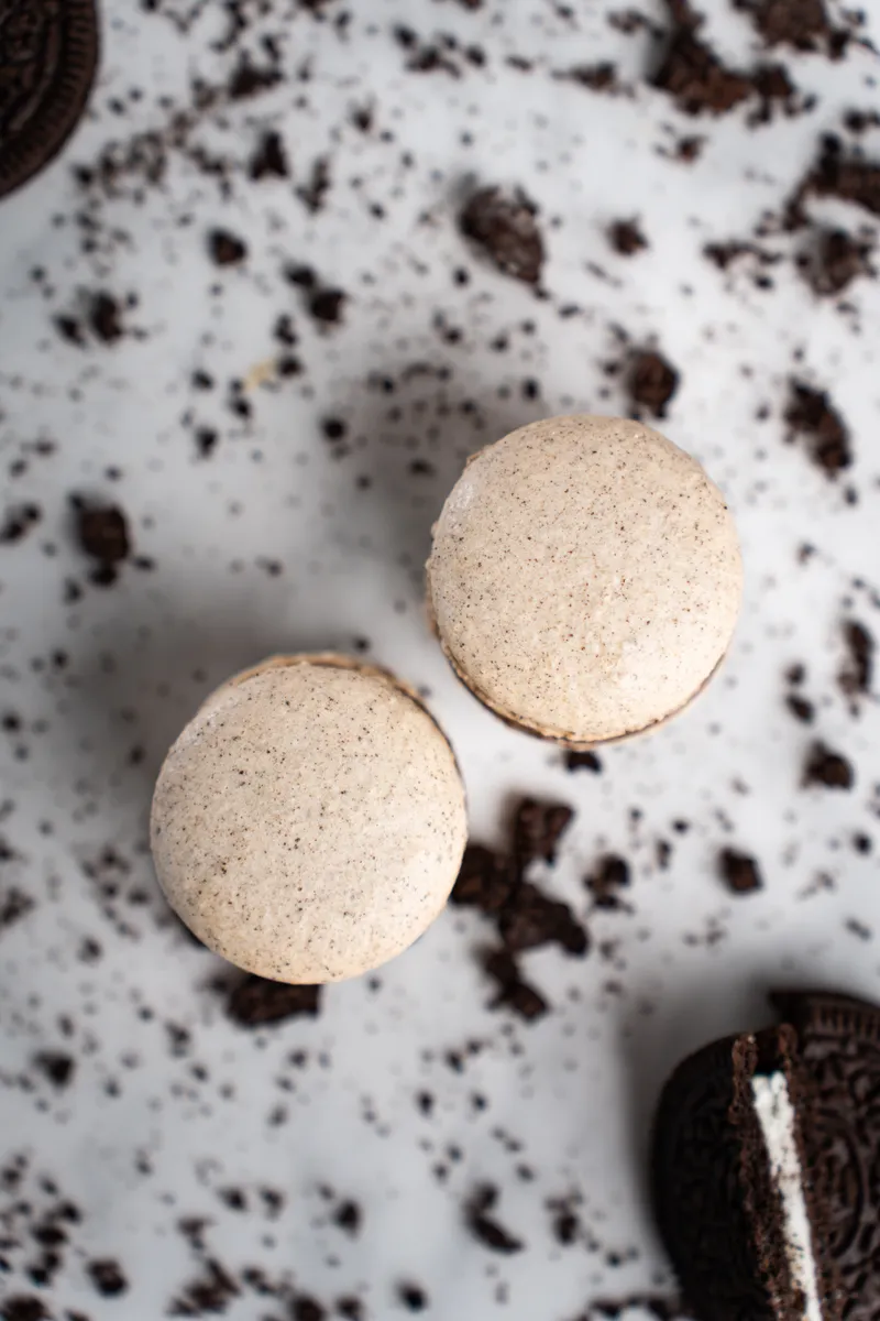 Oreo macarons speckled with cookie crumbs on white marble