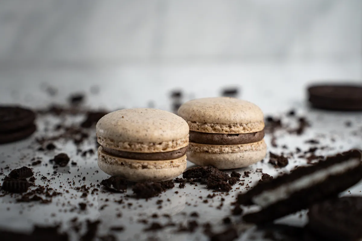 Oreo macarons speckled with cookie crumbs on white marble