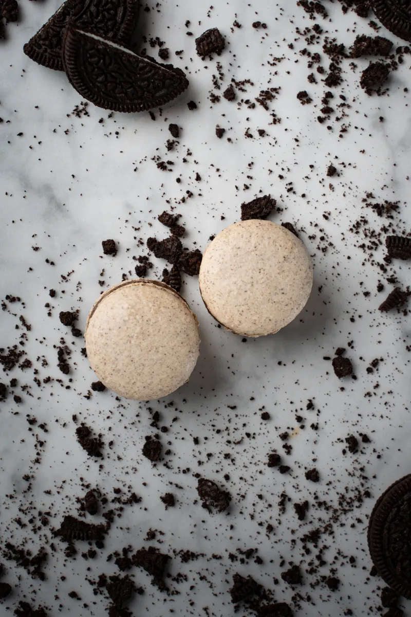 Oreo macarons speckled with cookie crumbs on white marble