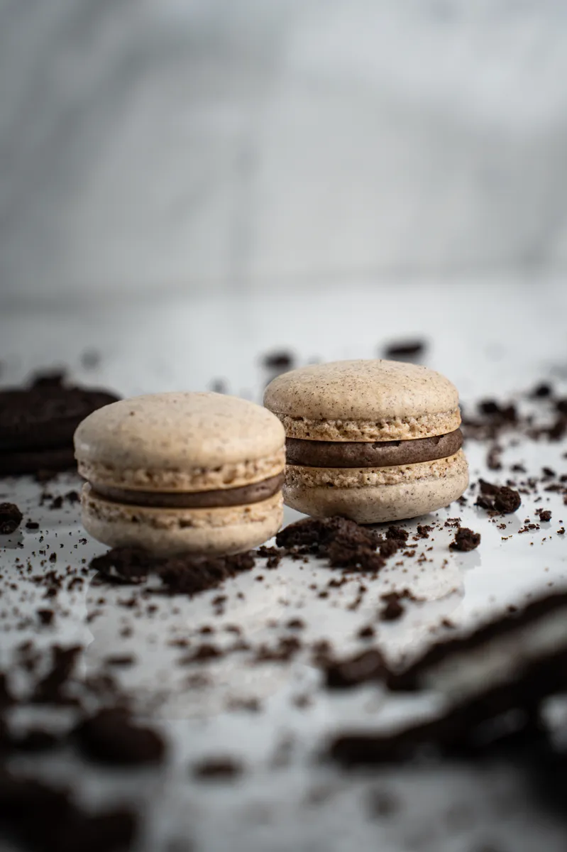 Oreo macarons speckled with cookie crumbs on white marble