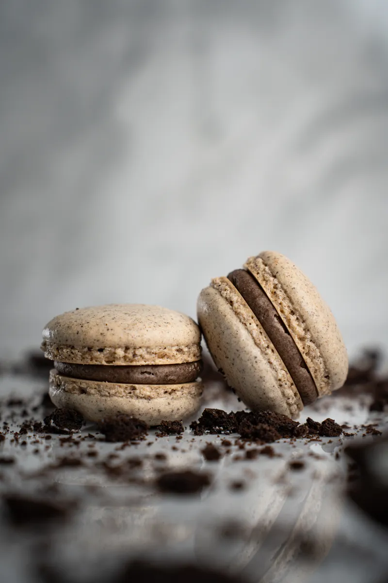 Oreo macarons speckled with cookie crumbs on white marble