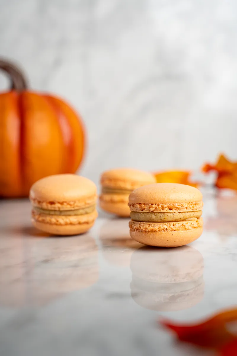 Orange pumpkin spice macarons on marble with a small pumpkin behind them