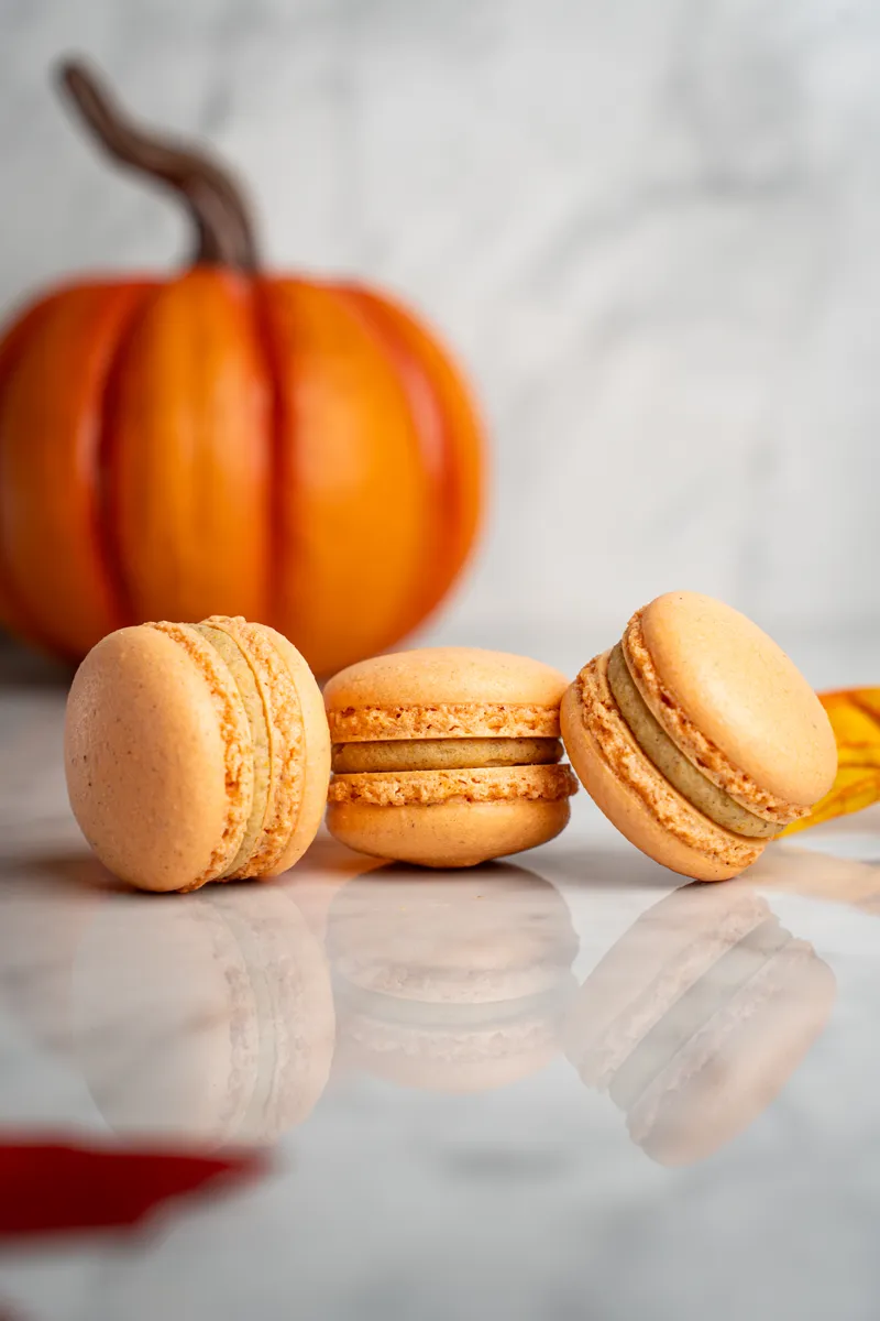 Orange pumpkin spice macarons on marble with a small pumpkin behind them