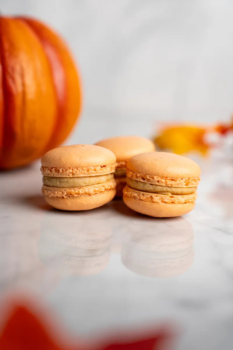 Orange pumpkin spice macarons on marble with a small pumpkin behind them