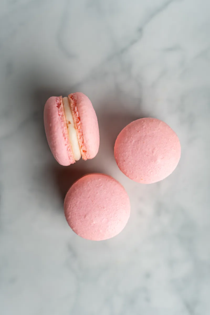 Pink raspberry cheesecake macarons with cream filling on white marble