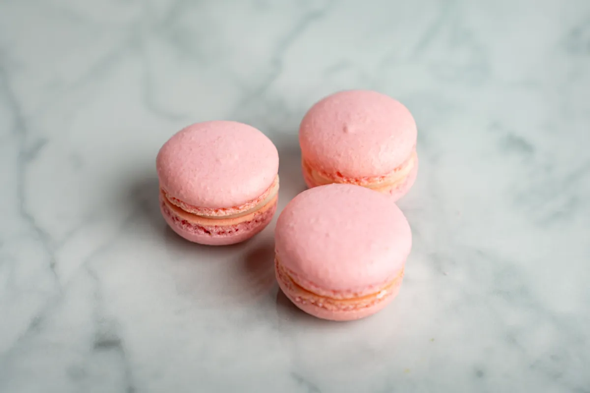 Pink raspberry cheesecake macarons with cream filling on white marble