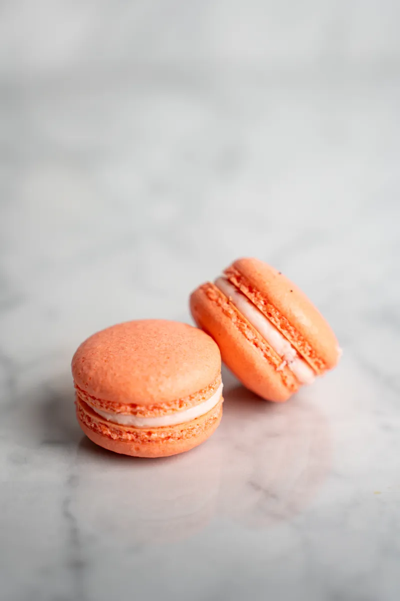 Coral strawberry macarons with cream filling on white marble