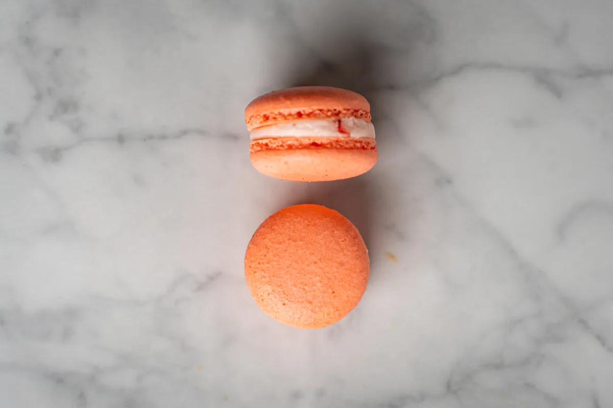 Coral strawberry macarons with cream filling on white marble