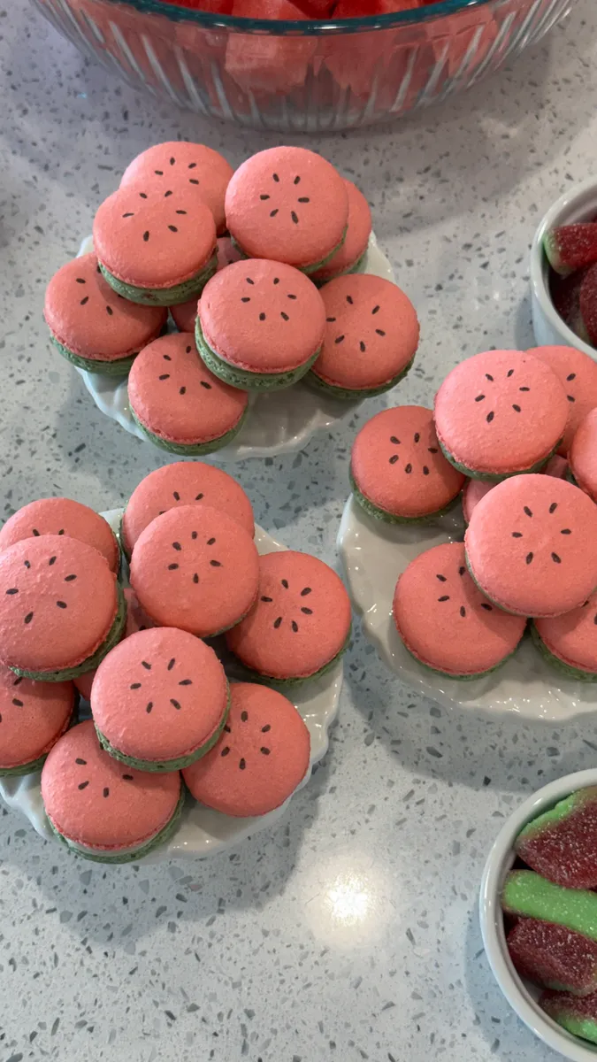 Watermelon macarons with pink tops, green shells, and seed details
