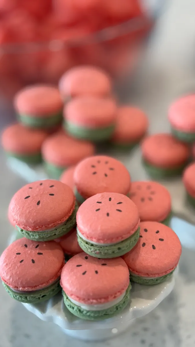 Watermelon macarons with pink tops, green shells, and seed details